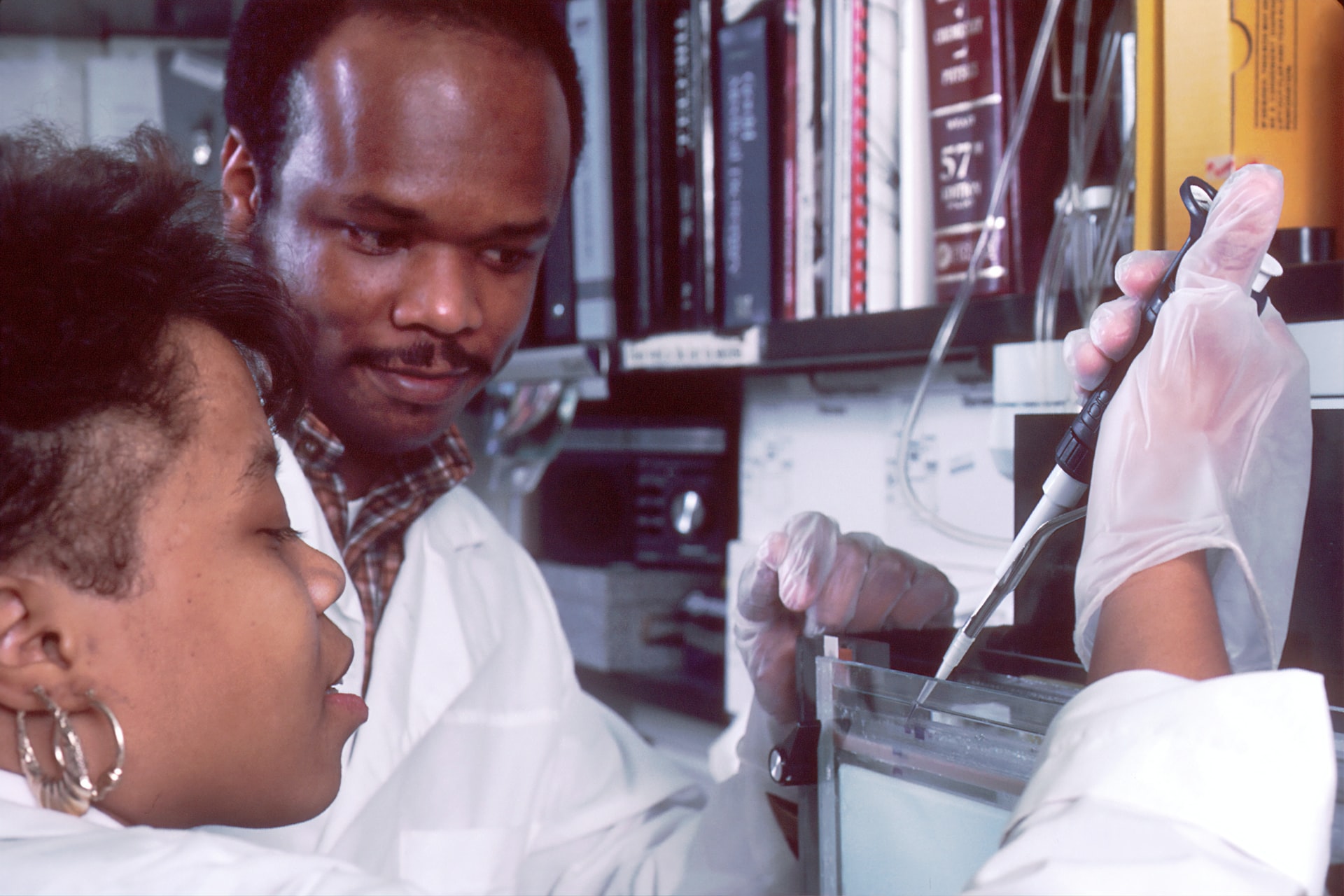 Two people in laboratory coats using a scientific looking apparatus